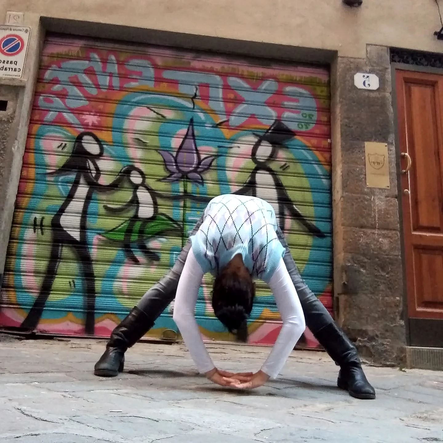 Nunzia piegata in avanti davanti a una saracinesca coperta di graffiti colorati, in una strada di Firenze